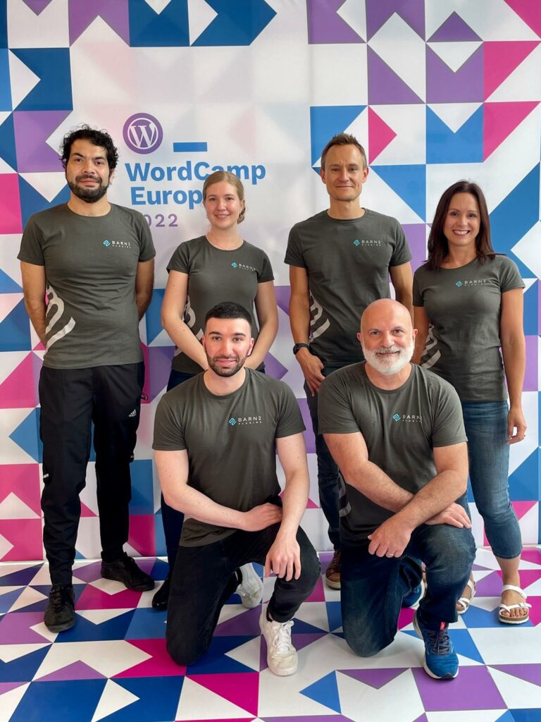 6 members of Barn2 team wearing Barn2 T-shirts and posing in front of WordCamp Europe photo wall